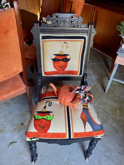 a pumpkin-shaped teapot on a halloween-themed chair